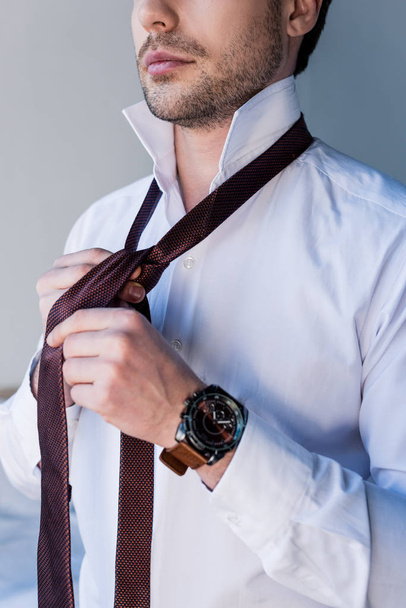 cropped view of confident man in white shirt putting tie on  - Valokuva, kuva