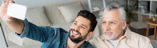 colpo panoramico di figlio barbuto felice prendendo selfie con padre allegro in pensione a casa
 - Foto, immagini