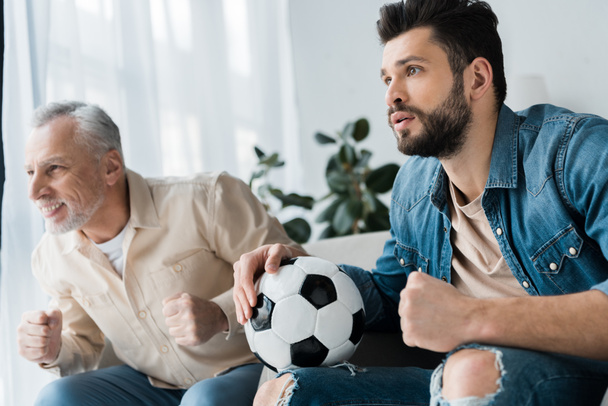 happy retired man watching championship and cheering with bearded son holding football  - Photo, Image
