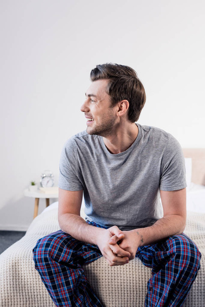 good-looking cheerful man sitting on bedding at home and looking away - Fotoğraf, Görsel