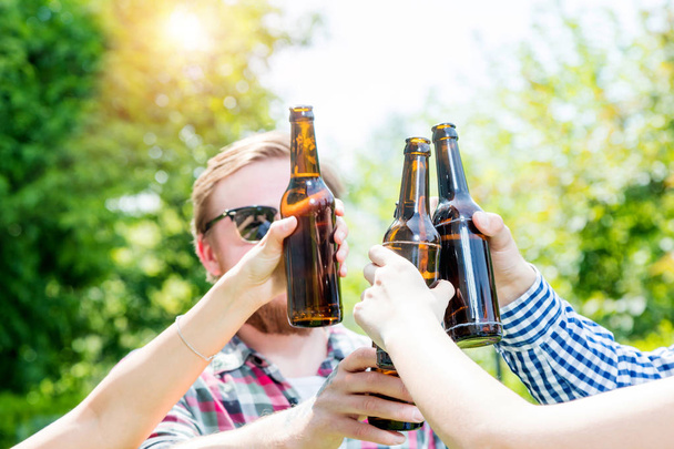 happy young friends clinking beer bottles outdoors at summertime - Foto, Imagem