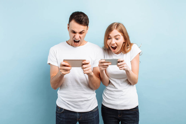 Young excited couple standing , playing games on mobile phones,  - 写真・画像