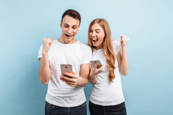 Photo of excited people, men and women, happily showing a gesture of victory and success, holding smartphones in their hands - Photo, Image