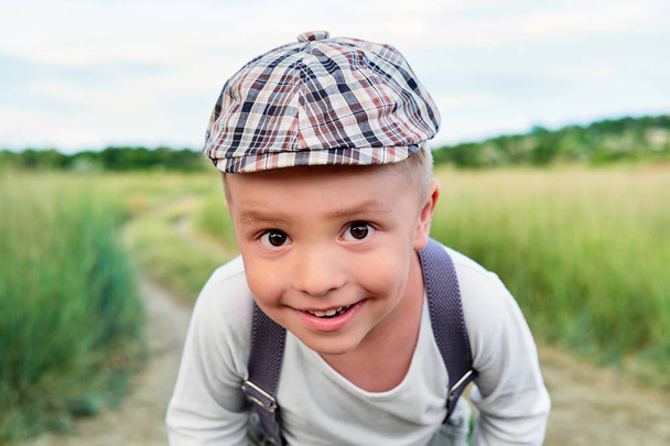 Funny happy child close-up. Attractive little boy looks into the camera with interest. Little kid smiling wears stylish cap, summer day. Pleased portrait. - Fotoğraf, Görsel