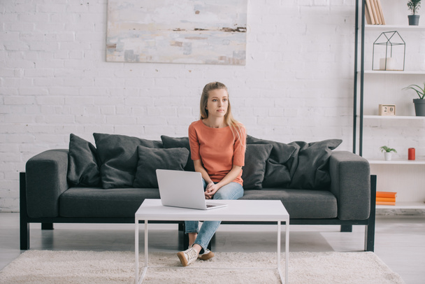 beautiful blonde freelancer sitting on sofa near laptop at home  - Foto, Imagen