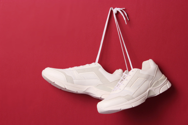 Moderne trendy sneakers hangen aan veters op een gekleurde achtergrond. Casual schoenen, sportschoenen. Plaats om tekst in te voegen. - Foto, afbeelding