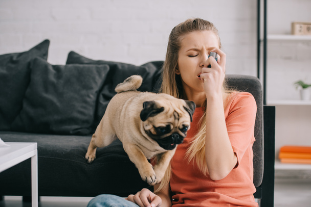 beautiful blonde woman allergic to dog using inhaler near pug at home  - Fotó, kép
