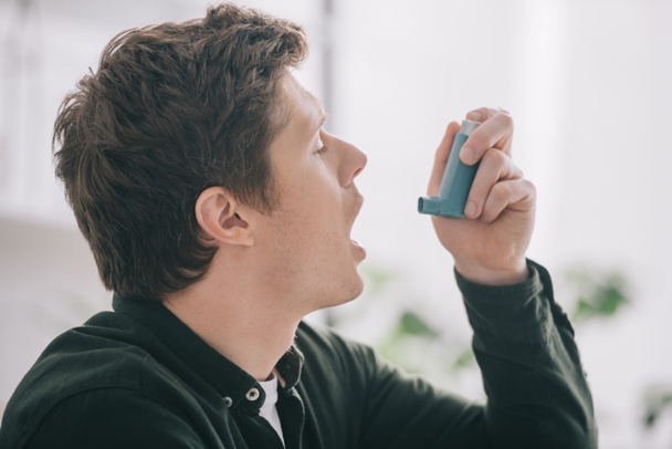 side view of handsome man using inhaler at home  - Photo, Image