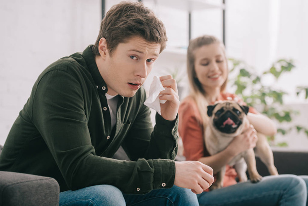 selective focus of handsome man allergic to dog looking at camera while holding tissue near cheerful girl with pug  - Zdjęcie, obraz