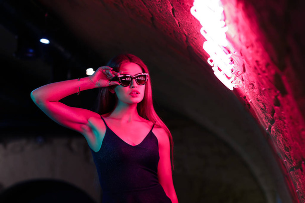 Portrait of beautiful young woman standing near neon lighting on wall - Foto, afbeelding