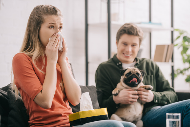 selective focus of woman allergic to dog sneezing near cheerful man with pug   - Valokuva, kuva