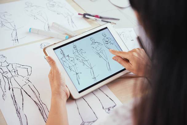 von oben Aufnahme eines anonymen Modedesigners mit modernem Tablet und beim Betrachten menschlicher Figurenskizzen am Tisch im Atelier - Foto, Bild