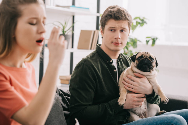 selective focus of man holding adorable pug and looking at girl allergic to dog using inhaler  - Fotoğraf, Görsel