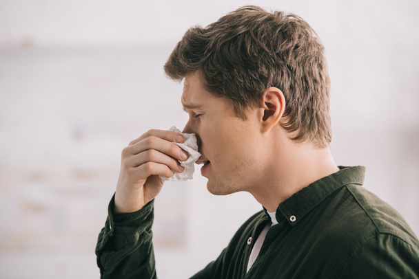 handsome man holding tissue and sneezing with closed eyes  - Фото, изображение