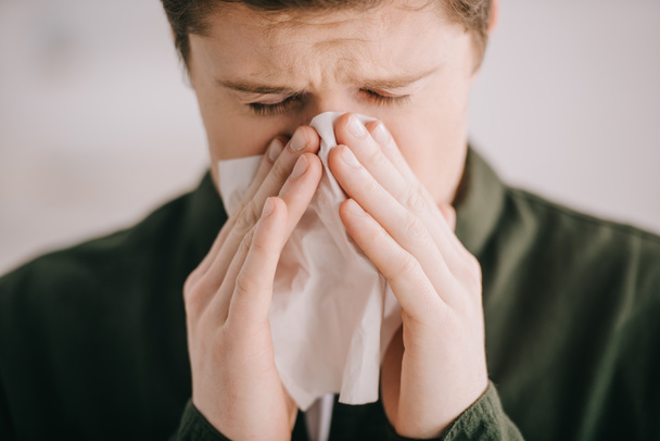 close up of man sneezing in tissue at home  - Photo, Image