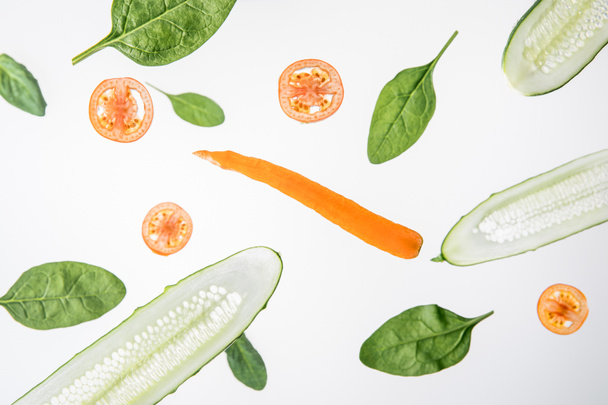 sliced cucumbers, tomatoes, carrot and green spinach leaves on grey background - 写真・画像