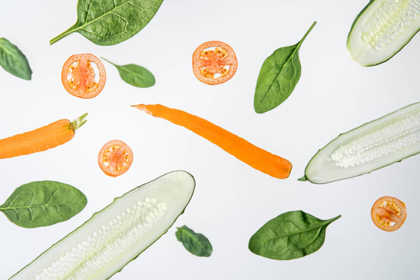 sliced cucumbers, tomatoes, carrots and green spinach leaves on grey background - 写真・画像