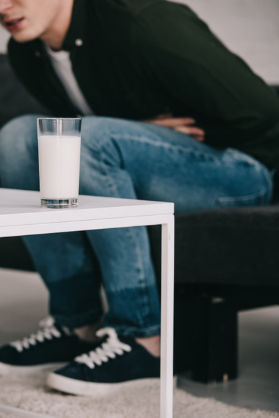 περικοπεί θεώρηση του ανθρώπου που κρατώντας το στομάχι και να κάθεται κοντά σε τραπεζάκι με ποτήρι γάλα  - Φωτογραφία, εικόνα