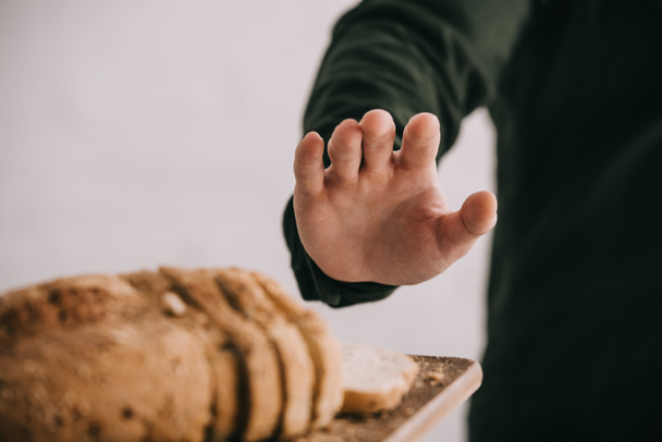 bijgesneden beeld van de mens in de buurt van snijplank gebaren met gesneden brood geïsoleerd op grijs  - Foto, afbeelding