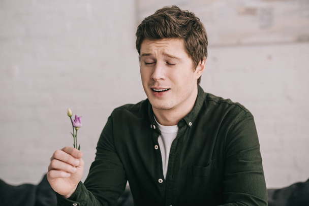 handsome man holding flower and sneezing at home  - Zdjęcie, obraz