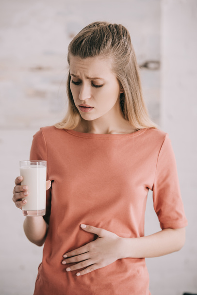 aantrekkelijke vrouw met lactose-intolerantie kijken glas melk  - Foto, afbeelding