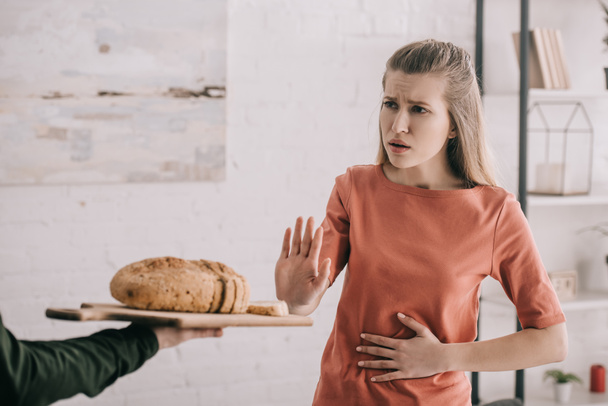 cropped view of man holding cutting board with bread near upset blonde woman with gluten allergy  - Фото, зображення