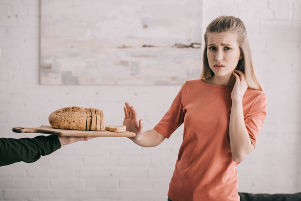 levágott képe ember tartja a vágódeszka, szeletelt kenyér közelében szomorú szőke nő glutén allergia  - Fotó, kép