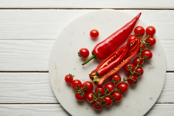 Top view of chili peppers and cherry tomatoes on wooden surface - 写真・画像