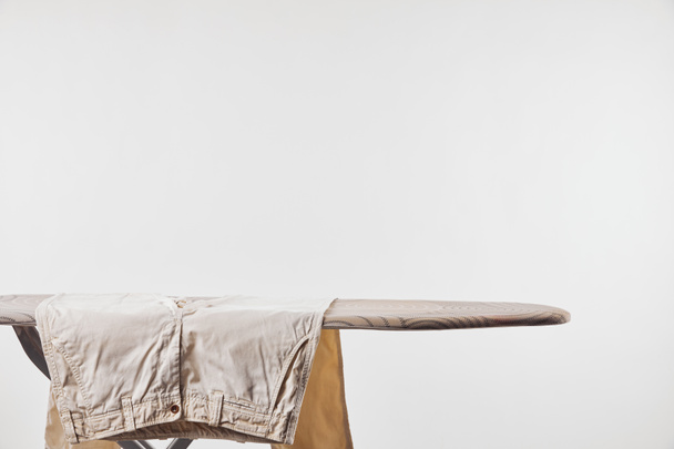Pantalones masculinos beige en tabla de planchar aislados en gris
 - Foto, imagen