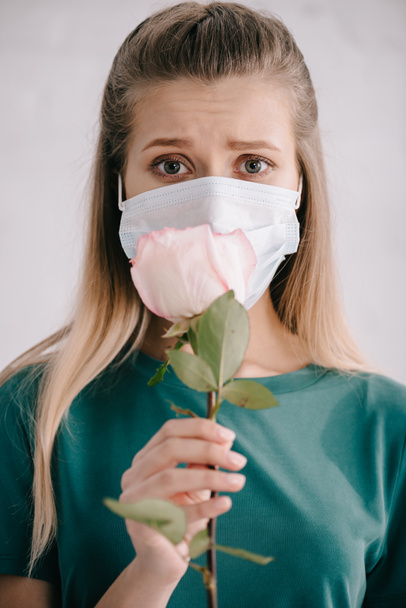 enfoque selectivo de la mujer rubia en máscara médica sosteniendo rosa en la mano
 - Foto, Imagen