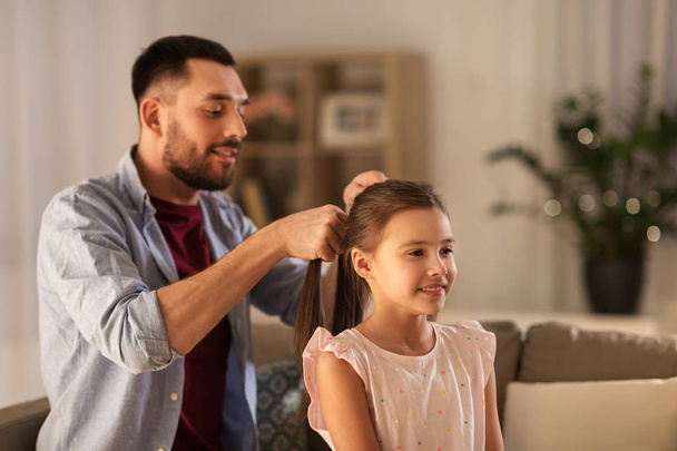 father braiding daughter hair at home - Фото, изображение