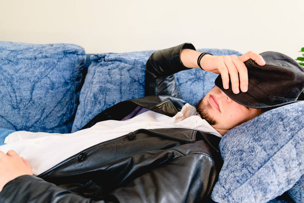 Νεαρός άνδρας κουρασμένος από την εργασία κάνει ένα διάλειμμα για έναν υπνάκο στον καναπέ, εμείς - Φωτογραφία, εικόνα