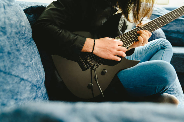 Νεαρός παίζει του συνεδρίαση μαύρη ηλεκτρική κιθάρα και απολαμβάνοντας - Φωτογραφία, εικόνα