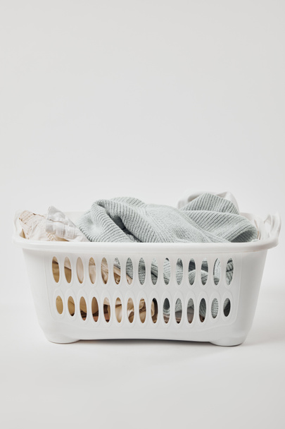 Cesta de lavandaria de plástico branco com roupas sujas em cinza
 - Foto, Imagem