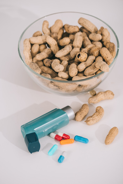 glass bowl with nutritious peanuts near blue inhaler and pills on grey  - Фото, зображення