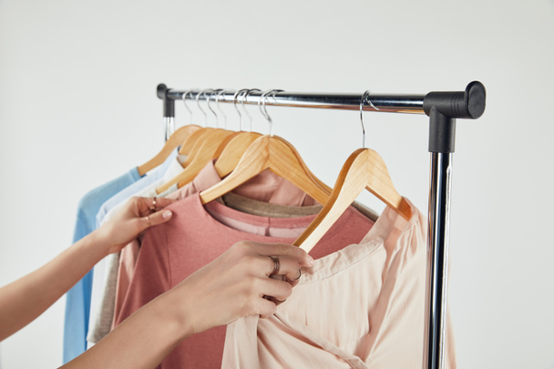 Partial view of woman touching clothes on wooden hangers isolated on grey - Photo, Image