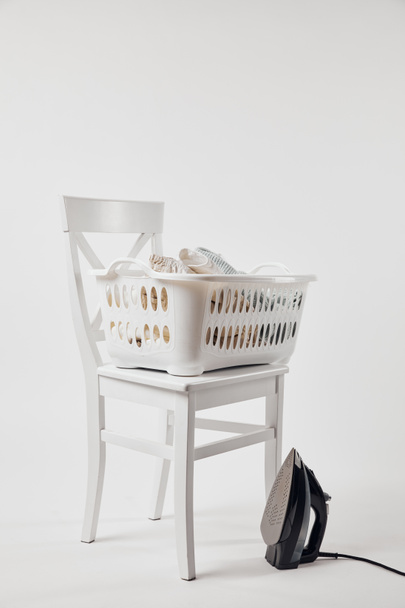 Λευκή καρέκλα, καλάθι πλυντηρίων με ρούχα και σίδερο σε γκρι - Φωτογραφία, εικόνα
