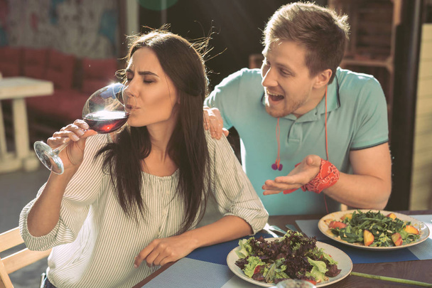 Resoluta menina de cabelos escuros bebendo vinho de vidro, enquanto seu namorado balançando-a
 - Foto, Imagem