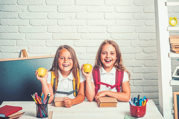 Back to school and home schooling. Friendship of small sisters in classroom at knowledge day. Little girls eat apple at lunch break. School time of girls. Happy school kids at lesson in september 1 - Φωτογραφία, εικόνα