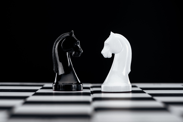selective focus of chessboard with white and black knights isolated on black - Foto, Bild