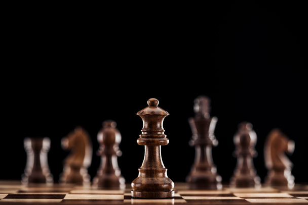 selective focus of brown wooden queen on chessboard isolated on black - Foto, Imagen