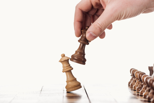 partial view of man holding brown queen near beige queen on wooden chessboard isolated on white - Photo, Image