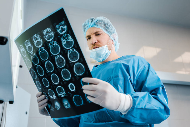 low angle view of doctor in medical cap and uniform holding x-ray in clinic  - Valokuva, kuva
