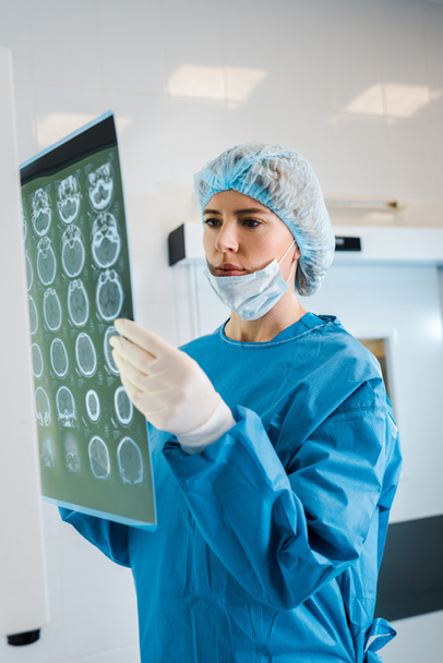 attractive doctor in medical cap and uniform holding x-ray in clinic  - Photo, Image