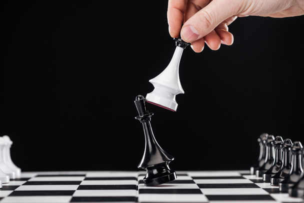 Обрезанный вид человека, делающего движение с королевой на шахматной доске, изолированной на черном
 - Фото, изображение