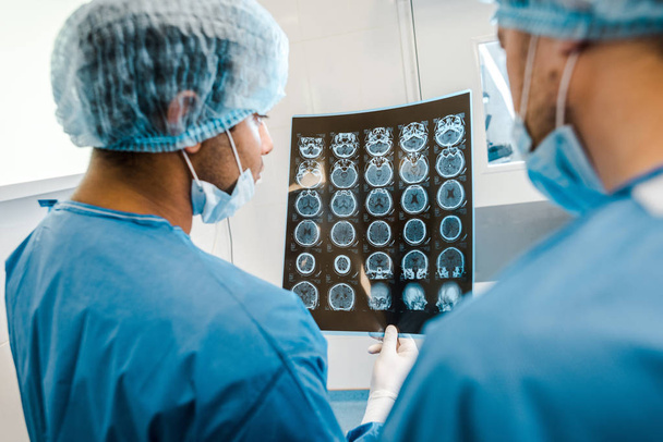 vista posterior de los médicos en uniformes y máscaras médicas mirando rayos X
 - Foto, Imagen
