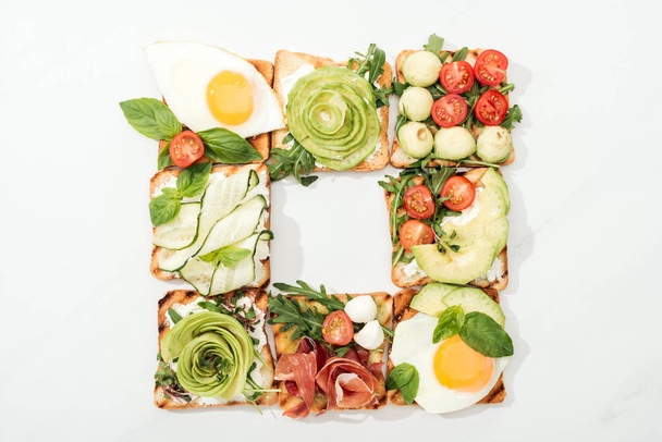 Top view of toasts with cut vegetables, fried eggs and prosciutto on white surface - Fotografie, Obrázek