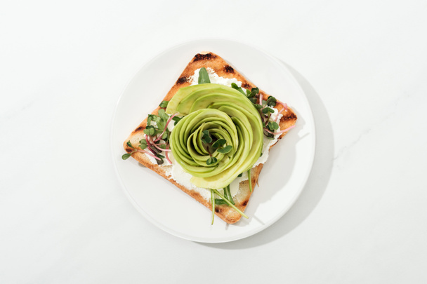 Top view of toast with sliced avocado and garden cress on plate on white surface - Photo, Image