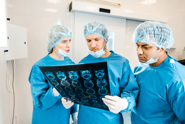 knappe en mooie artsen in uniformen en medische maskers praten over x-ray  - Foto, afbeelding