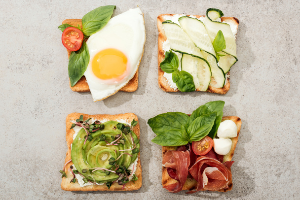 Top view of toasts with vegetables, fried egg and prosciutto on textured surface - Foto, Imagen